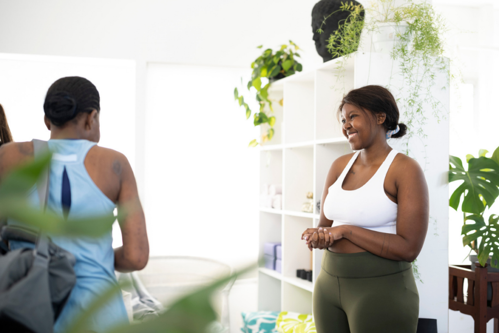 Yoga teacher warmly chatting with a student at the end of class in a bright, welcoming yoga studio.